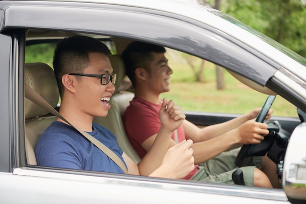 Seitenansicht von zwei sorglosen Kerlen, die im Auto betriebsbereit zu einer Autoreise sitzen