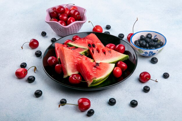 Seitenansicht Wassermelonenscheiben auf einem Teller mit Blaubeeren und Kirschen