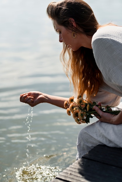 Kostenloses Foto seitenansichtfrau, die durch den see sitzt