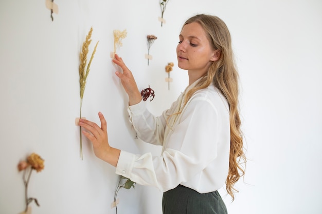 Seitenansichtfrau, die getrocknete Blumen an Wand setzt