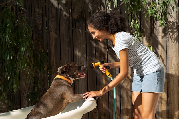 Kostenloses Foto seitenansichtfrau, die hund mit schlauch wäscht