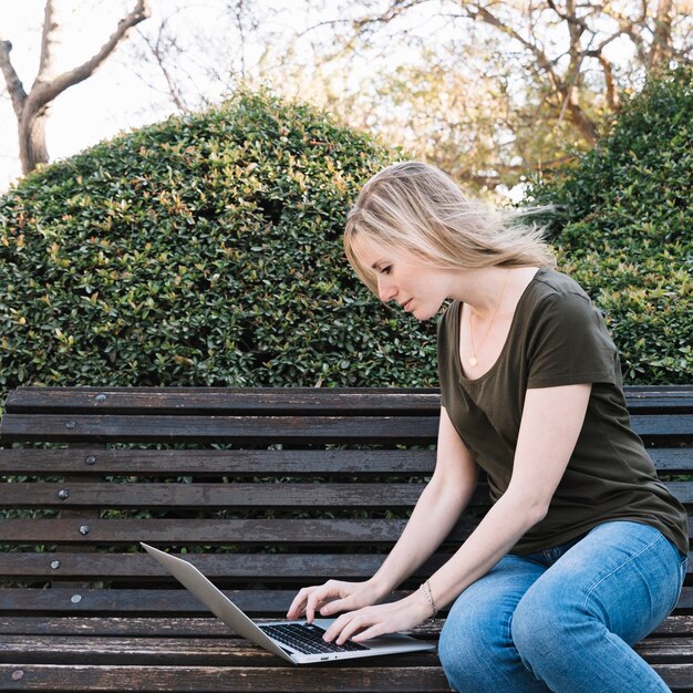 Seitenansichtfrau, die Laptop auf Bank verwendet