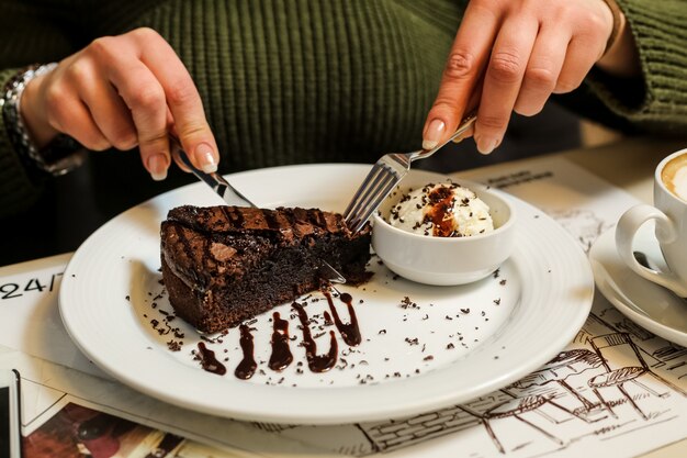 Seitenansichtfrau, die Schokoladenkuchen mit Eiscreme und Schokoladenglasur auf einem Teller isst