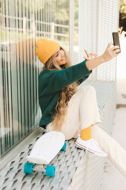 Seitenansichtfrau, die selfie mit Skateboard nimmt