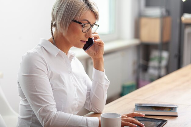 Seitenansichtfrau im Büro sprechend über Telefon