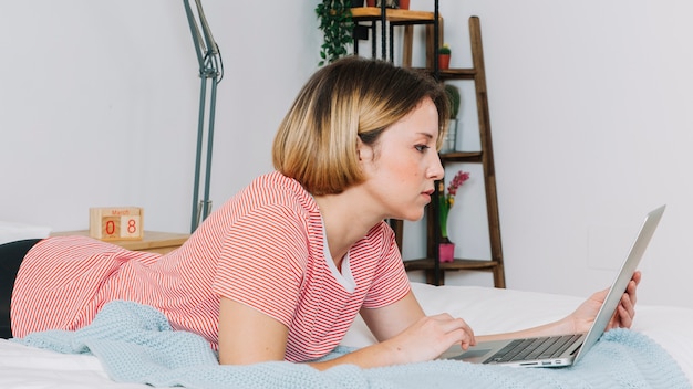 Seitenansichtfrau mit Laptop auf Bett