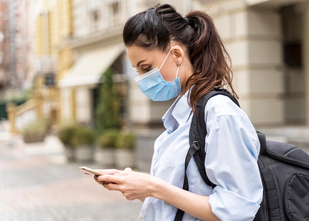 Kostenloses Foto seitenansichtfrau mit medizinischer maske, die ihr telefon prüft