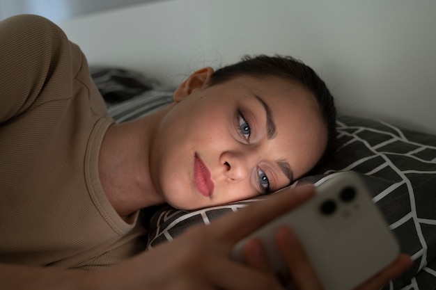 Seitenansichtmädchen, das mit Smartphone im Bett liegt