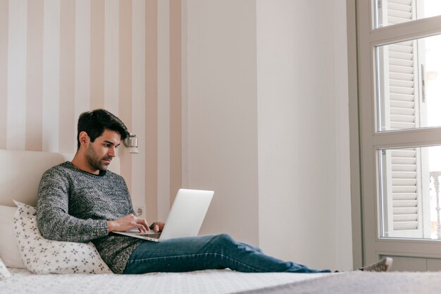 Seitenansichtmann Surfen Laptop auf dem Bett