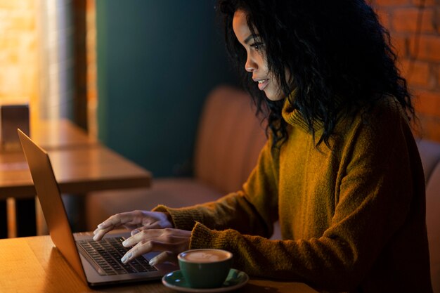 Seitenansichtsfrau, die an ihrem Laptop in einem Kaffeehaus arbeitet
