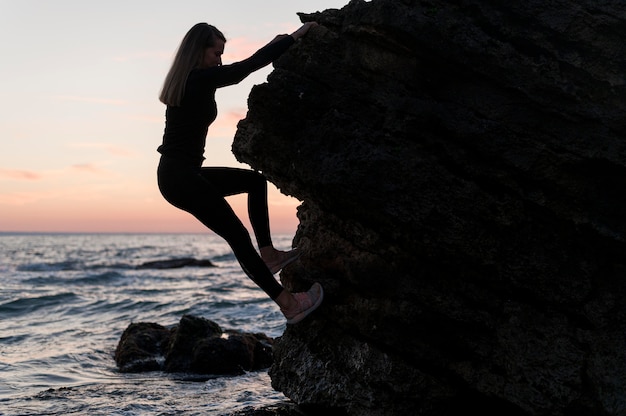 Seitenansichtsfrau, die einen Felsen nahe dem Ozean klettert