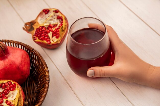 Seitenansichtsfrau, die Glas Granatapfelsaft mit Granatäpfeln in einem Korb auf einer weißen Wand hält