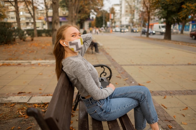 Seitenansichtsfrau mit der medizinischen Maske, die auf einer Bank sitzt