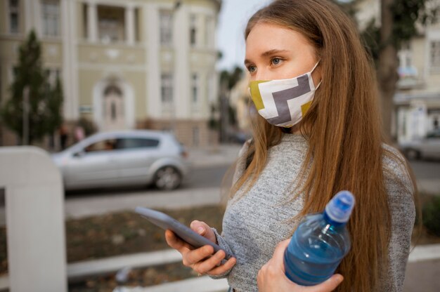 Seitenansichtsfrau mit der medizinischen Maske, die eine Flasche Wasser hält