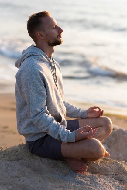 Seitenansichtsmann, der am Strand meditiert