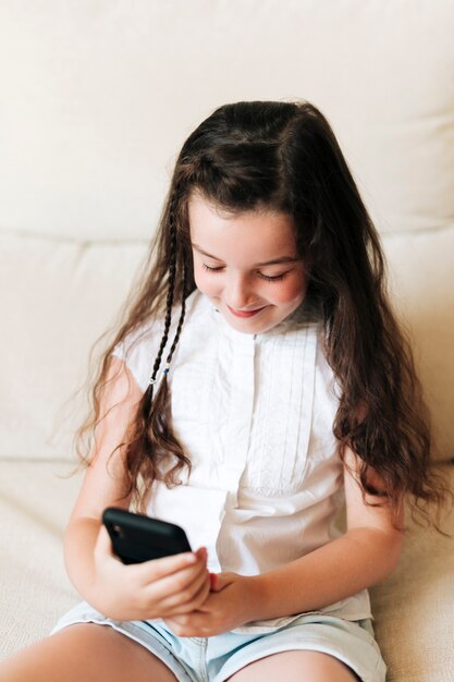 Seitenansichtsmileymädchen, das Telefon betrachtet