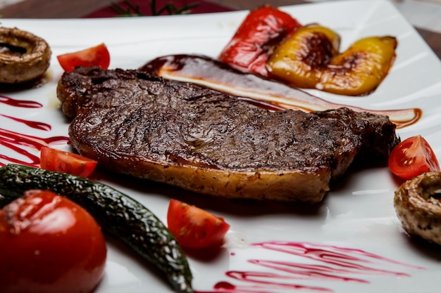 Seitenansichtssteak mit Tomate und gebratenen Pilzen und gebratenem Paprika im weißen Teller auf Holztisch