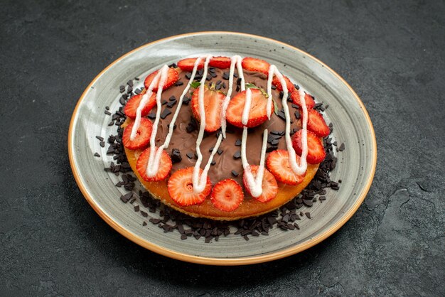 Seitennahaufnahme appetitlicher Kuchenkuchen mit Schokoladen- und Erdbeerstücken auf Teller in der Mitte des dunklen Tisches