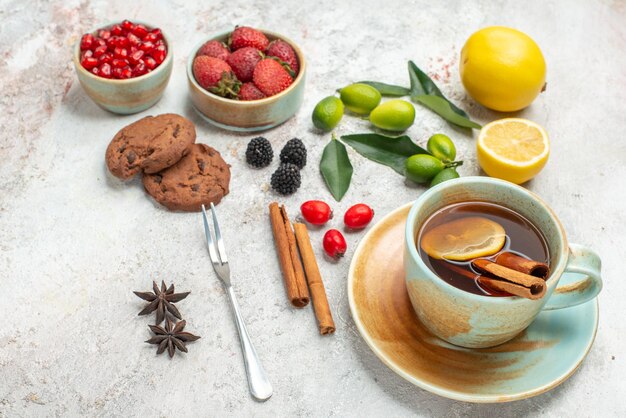 Seitennahaufnahme Beerenplätzchen Sternanisplätzchen Erdbeeren weiße Tasse Tee Zitrusfrüchte Zimtstangen Gabel auf dem Tisch