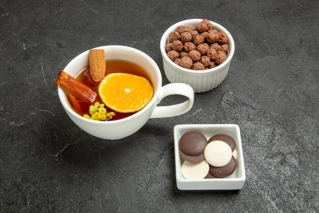 Seitennahaufnahme eine Tasse Tee-Hizelnüsse eine Tasse Tee mit Zimt und Zitrone und Schalen mit Schokolade und Haselnüssen auf dunklem Hintergrund