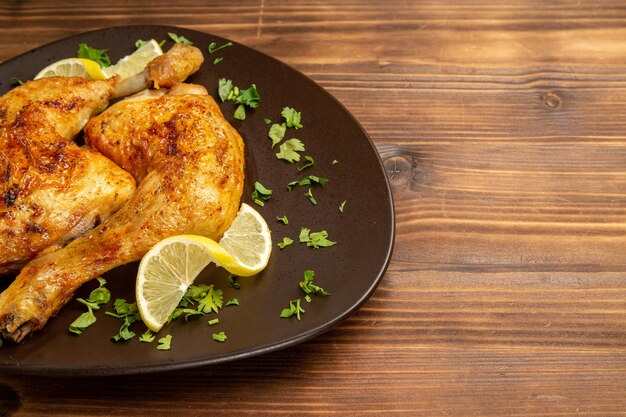 Seitennahaufnahme Hühnchen und Kräuter brauner Teller mit Hähnchenschenkeln mit Zitrone und Kräutern auf der linken Seite des dunklen Tisches