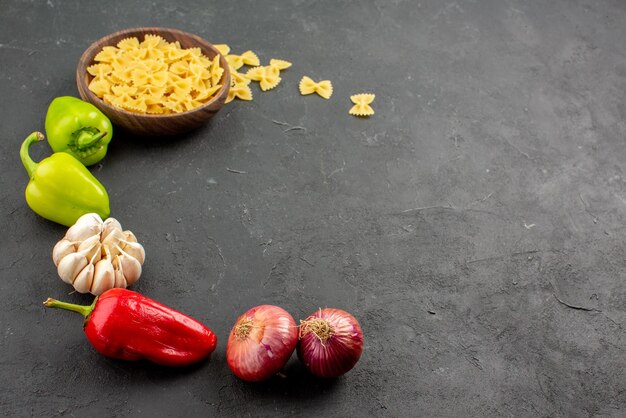 Seitennahaufnahme Nudeln und Gemüse Paprika Knoblauchzwiebel und Schüssel Nudeln sind in einem Kreis auf dem Tisch ausgelegt