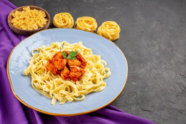 Seitennahaufnahme Pasta mit Soße appetitliche Pasta mit Soße und Fleisch auf dem Teller neben den verschiedenen Pastasorten auf der lila Tischdecke