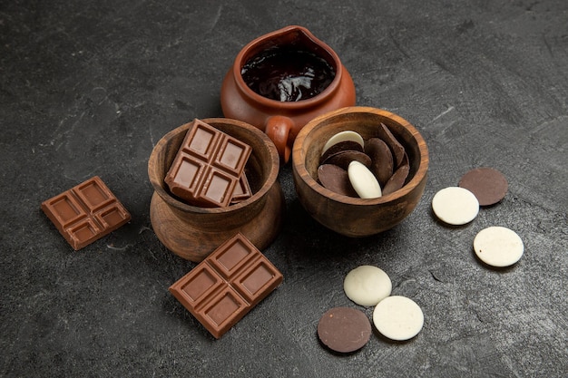 Seitennahaufnahme Schokoladenschokolade und Schokoladensauce in den Schalen auf dem schwarzen Tisch