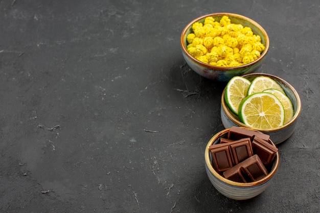 Seitennahaufnahme süßigkeiten in schalen schokoladenlimetten und gelbe bonbons in den weißen schalen an der dunklen wand