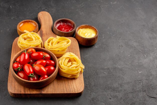 Seitennahaufnahme Tomaten und Nudeln Tomaten und Nudeln auf dem Küchenbrett neben den Soßenschüsseln auf dem Tisch