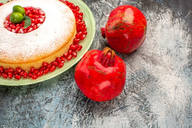 Seitennahaufnahmekuchen mit Granatäpfeln reifen Granatäpfeln und dem Teller eines appetitlichen Kuchens