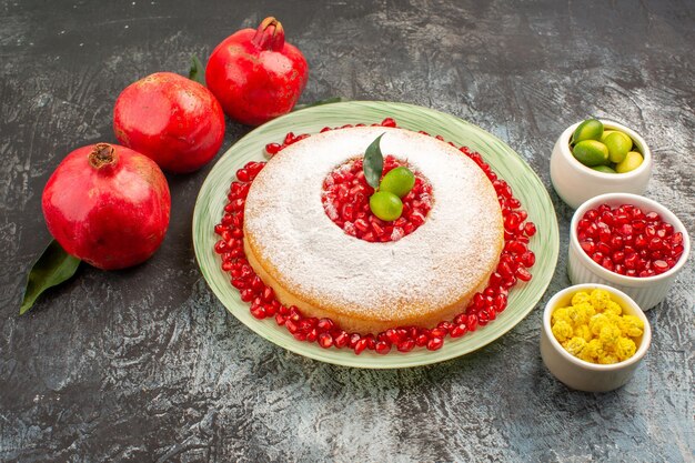 Seitennahaufnahmekuchen mit Granatapfelschalen mit Beeren ein appetitlicher Kuchen und drei Granatäpfel