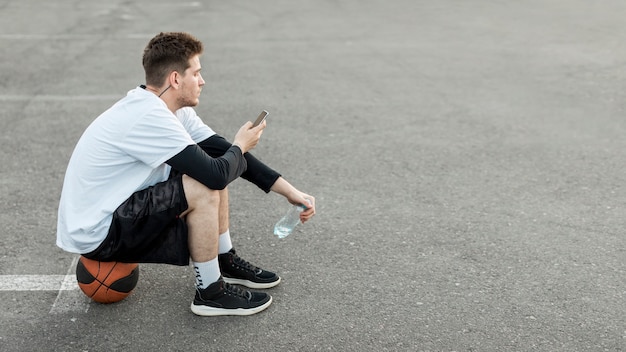 Kostenloses Foto seitlich basketballspieler, der sein telefon überprüft