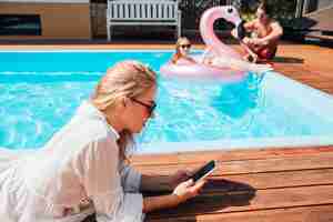 Kostenloses Foto seitlich frau, die ihr telefon am pool überprüft