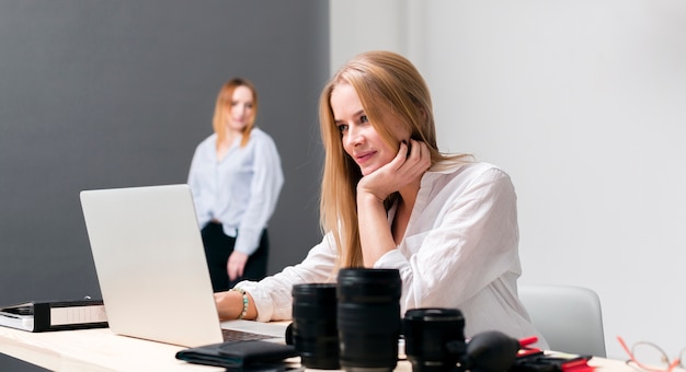 Seitlich nettes Mädchen, das Laptop und weibliches Baumuster im Hintergrund betrachtet