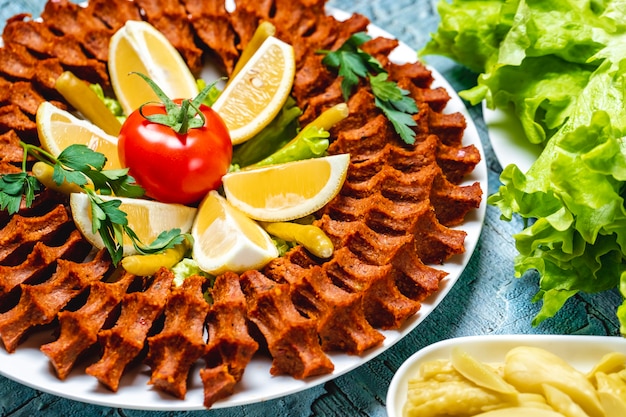 Seitliche Ansicht vegetarische Steak-Tartar-Kugeln mit Zitronengrünscheiben und frischen Tomaten auf einem Teller