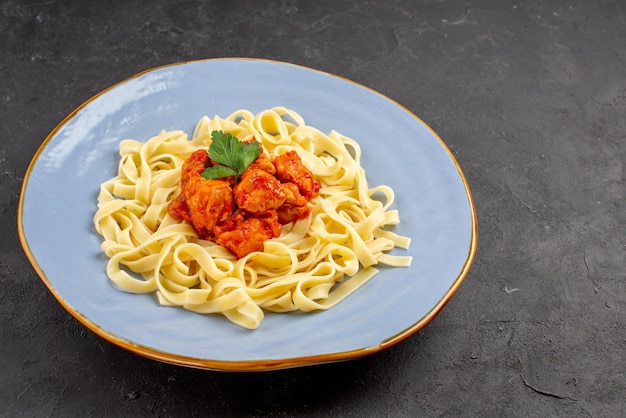 Kostenloses Foto seitliche nahaufnahme appetitanregendes essen appetitliche pasta mit soße und fleisch in der blauen platte auf dem dunklen tisch