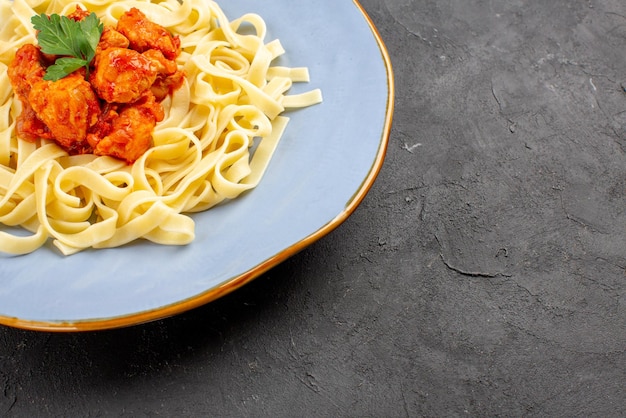 Seitliche nahaufnahme appetitanregendes essen leckere pasta mit fleisch und soße in der blauen platte auf dem dunklen tisch