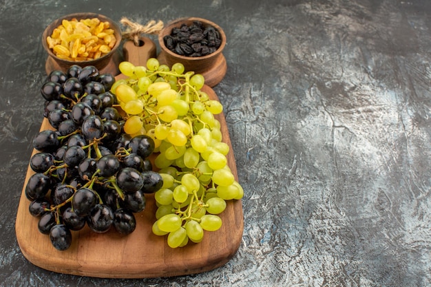Seitliche Nahaufnahme Früchte Bündel von grünen und schwarzen Trauben auf dem Brett Schalen mit getrockneten Früchten