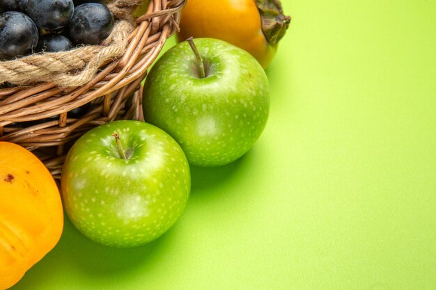 Seitliche Nahaufnahme Früchte grüne Äpfel Trauben von schwarzen Trauben Kaki auf dem grünen Tisch
