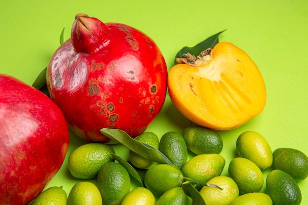 Seitliche Nahaufnahme Früchte rote Granatäpfel grün-gelbe Zitrusfrüchte Kaki auf dem Tisch