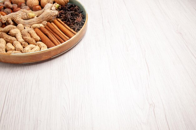 Seitliche Nahaufnahme Zimtstangen Erdnüsse Walnüsse Haselnüsse Sternanis und Zimt auf der Holzplatte auf dem weißen Tisch