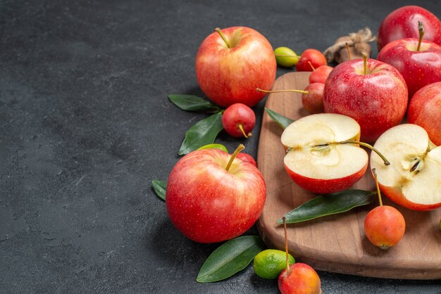 Seitliche Nahaufnahmefrüchte Früchte gelb-rote Kirschen mit Blättern Äpfel auf dem Brett Zitrusfrüchte