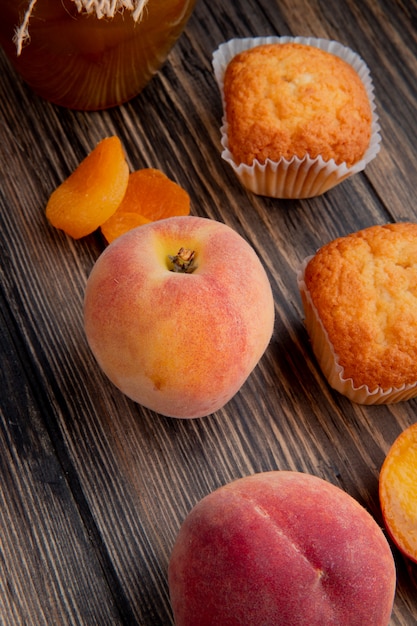Seitliche Sicht auf frische reife Pfirsich mit Muffins, getrockneten Aprikosen auf rustikalem Holz
