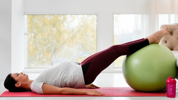 Seitwärts junge schwangere Frau, die auf Fitnessball ausübt