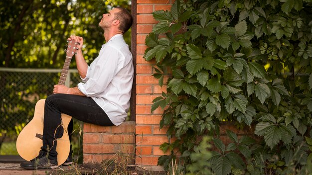 Seitwärts Mann, der mit seiner akustischen Gitarre draußen sitzt