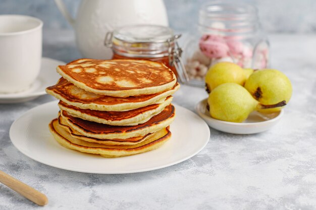 Selbst gemachtes Frühstück: Pfannkuchen im amerikanischen Stil, serviert mit Birnen und Honig bei einer Tasse Tee auf Beton. Draufsicht und Kopie