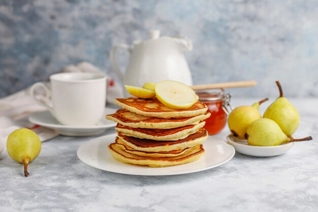 Selbst gemachtes Frühstück: Pfannkuchen im amerikanischen Stil, serviert mit Birnen und Honig bei einer Tasse Tee auf Beton. Draufsicht und Kopie