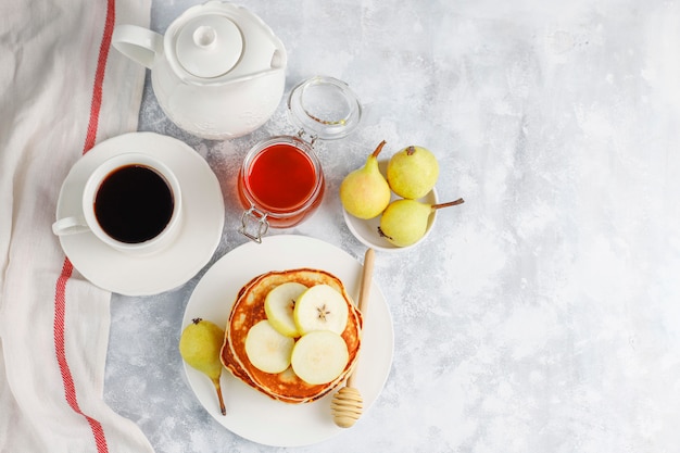 Selbst gemachtes Frühstück: Pfannkuchen im amerikanischen Stil, serviert mit Birnen und Honig bei einer Tasse Tee auf Beton. Draufsicht und Kopie
