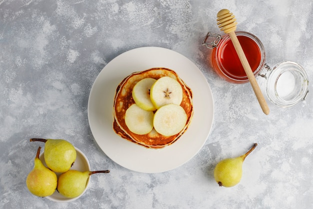 Selbst gemachtes Frühstück: Pfannkuchen im amerikanischen Stil, serviert mit Birnen und Honig bei einer Tasse Tee auf Beton. Draufsicht und Kopie